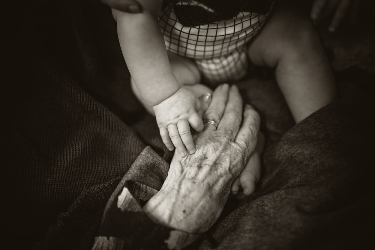 A baby’s small hand resting on an elderly person’s weathered hand